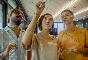 Drie personen schrijven hun ideeën op een transparant bord