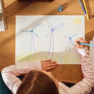 Top View: Little Girl Drawing Beautiful Wind Turbines that Look Like Flowers. On Sunny Day Smart Kid Imagining Our Planet as a Happy Place with Clean, Sustainable Green Energy for Everyone.