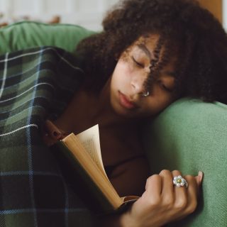 Om de verwarming niet aan te zetten heeft een jongedame een dekentje gepakt. Ze ligt op de bank te lezen.