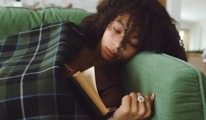 Om de verwarming niet aan te zetten heeft een jongedame een dekentje gepakt. Ze ligt op de bank te lezen.