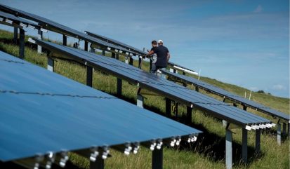 Twee mannen lopen tussen de zonnepanelen op een dijk