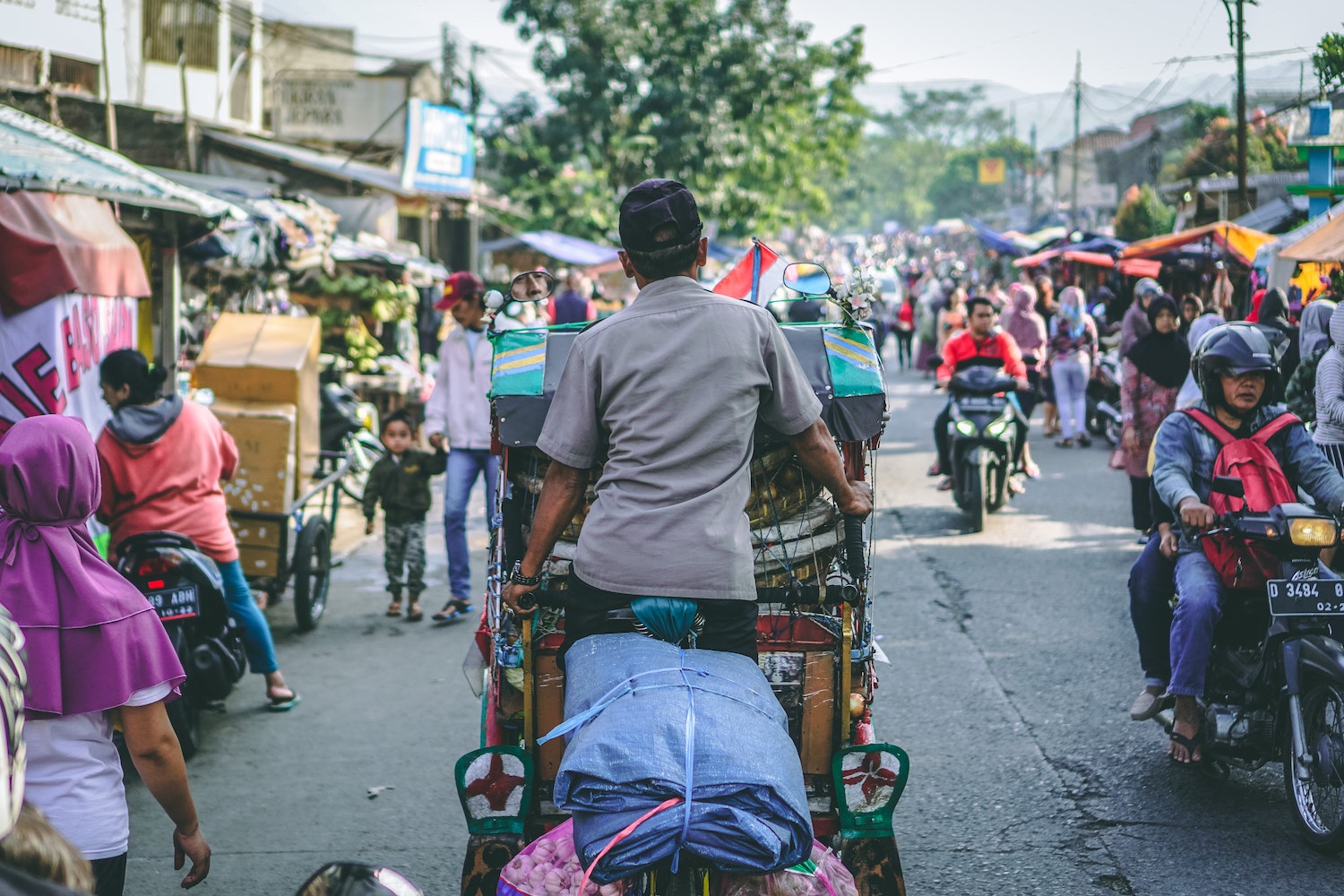 Energietransitie in Indonesië: een typische drukke straat met brommers, tuk-tuks en wandelende mensen langs marktkramen