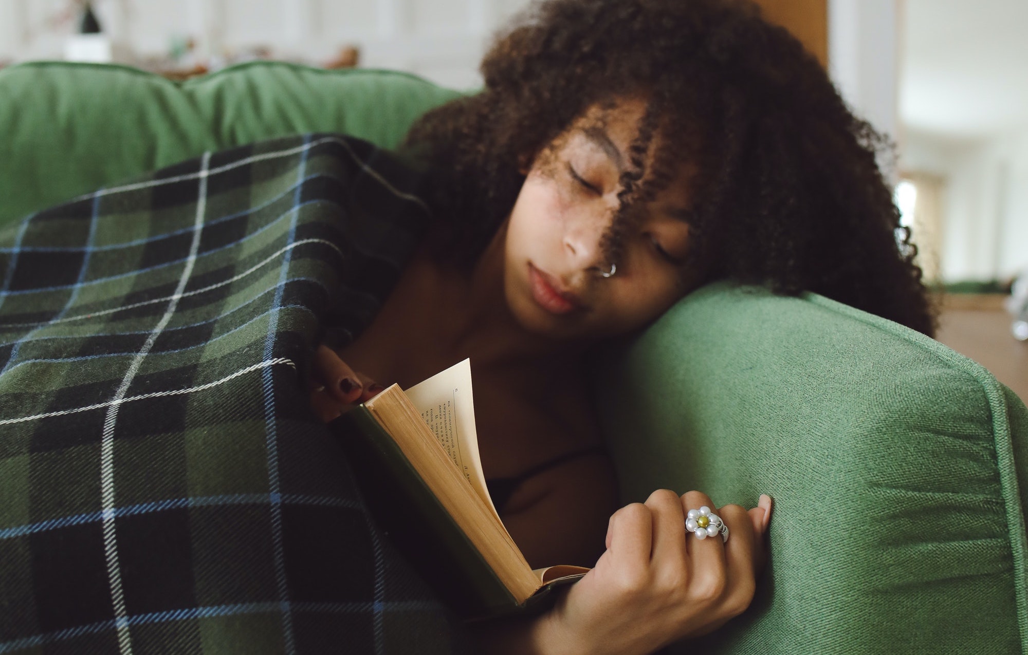 Om de verwarming niet aan te zetten heeft een jongedame een dekentje gepakt. Ze ligt op de bank te lezen.